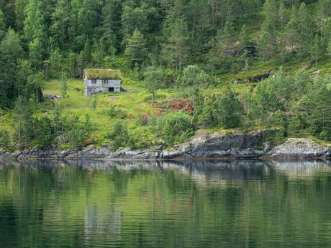 Hus med torvtak i skogkanten ved en rolig fjord